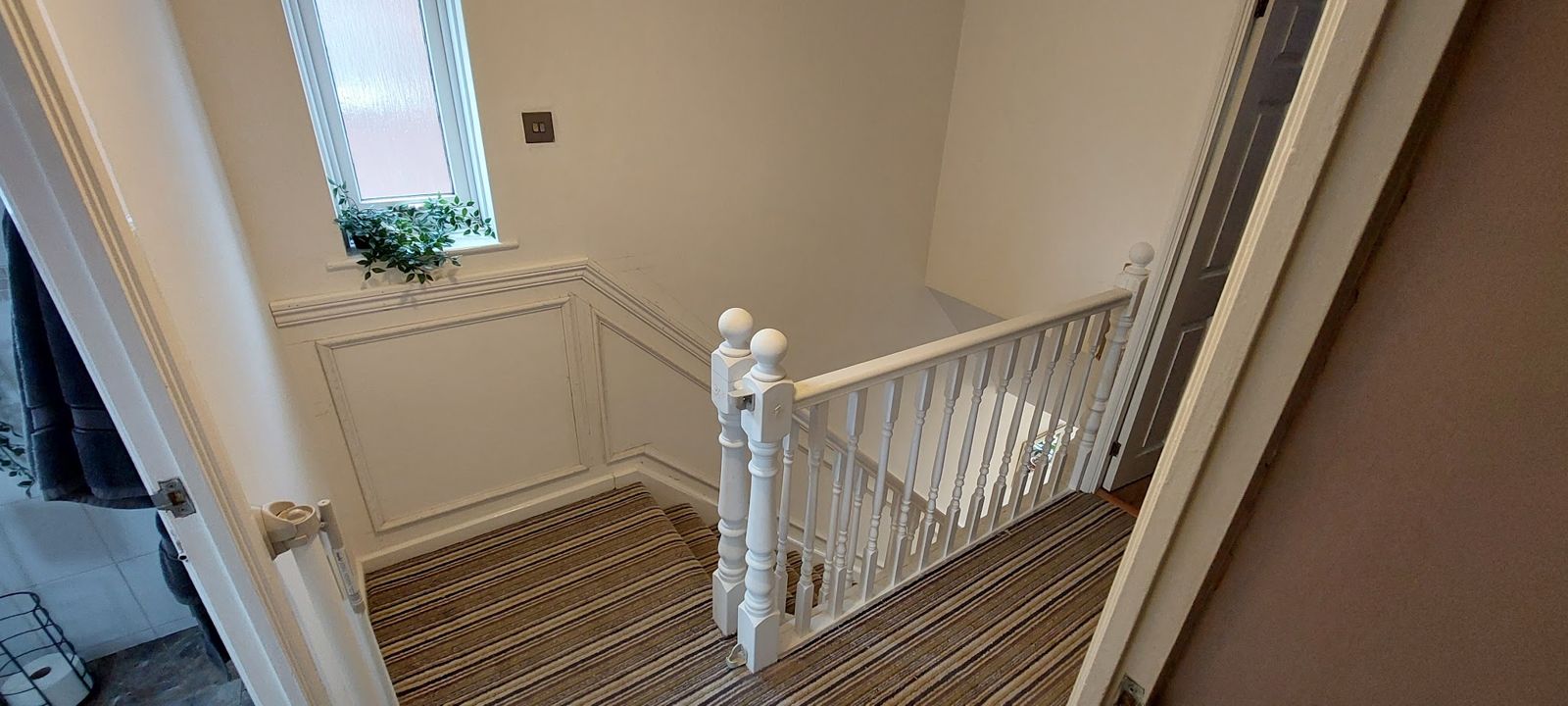 Landing with a white spindle balustrade and newel post beside wall panelling