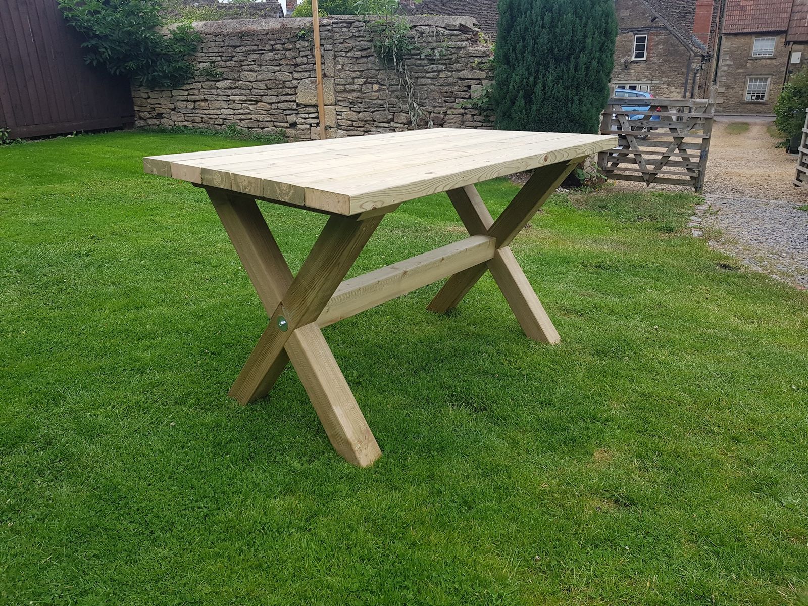 Cross-frame timber garden table on a lawn, with a Cotswold stone wall behind