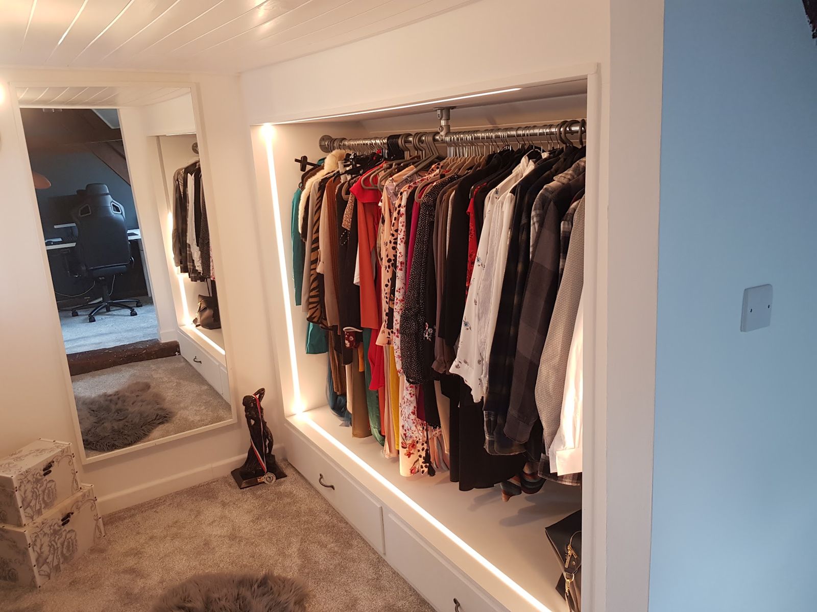 Walk-in wardrobe with a lit hanging rail and drawers below
