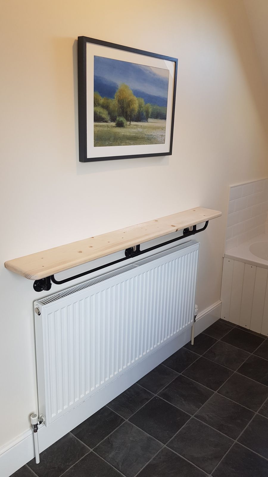 Timber shelf fixed over a radiator on black pipe brackets, with a framed picture above